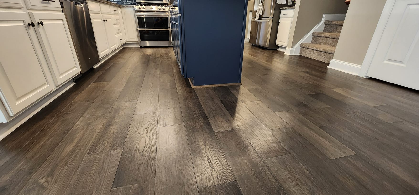 Wide-plank hardwood floors installed in a kitchen with a navy island by Frankie D&rsquo;s Flooring