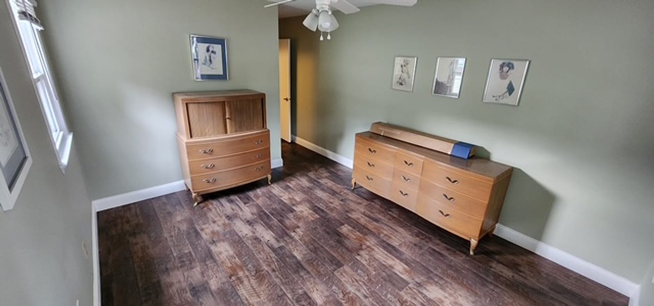 Dark plank flooring under vintage oak dressers in a sage bedroom by Frankie D&rsquo;s Flooring